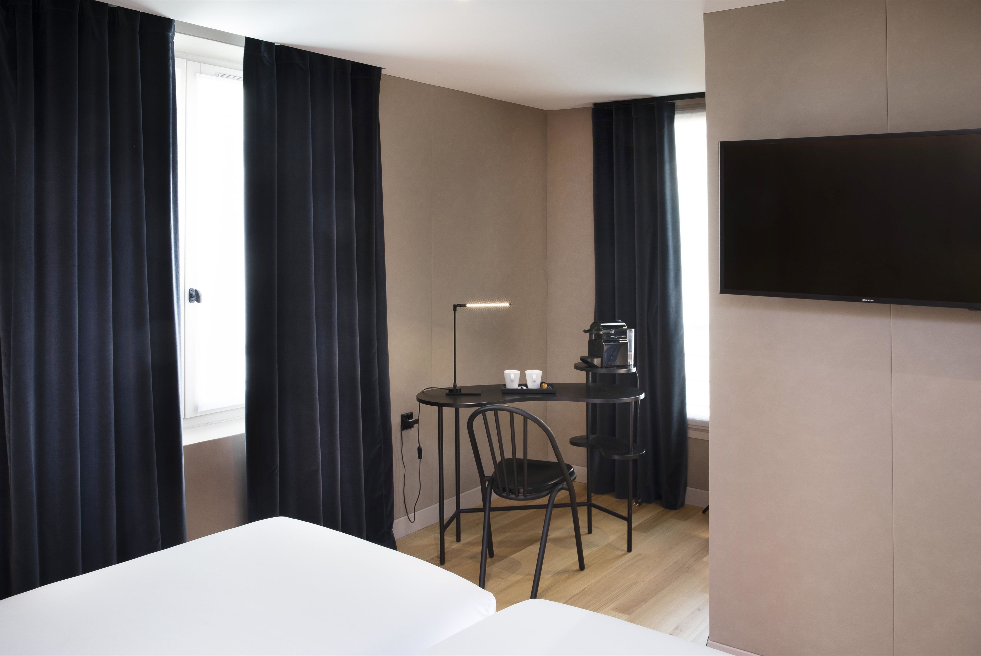 A hotel room with a bed, a desk with a chair, a flat-screen TV, and a window with curtains.