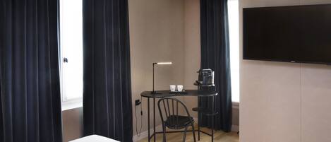 A hotel room with a bed, a desk with a chair, a flat-screen TV, and a window with curtains.