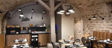 A cozy cafe with stone walls, wooden tables, and black chairs.