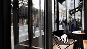 Un intérieur moderne avec de grandes fenêtres, un fauteuil en cuir noir et une petite table agrémentée d’une plante.