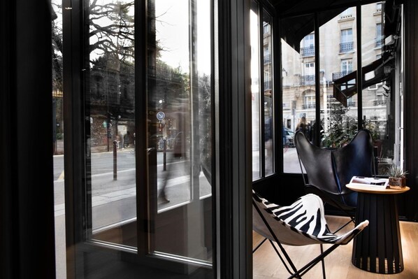 Een modern interieur met grote ramen, een zwarte leren fauteuil en een klein tafeltje met een plant.