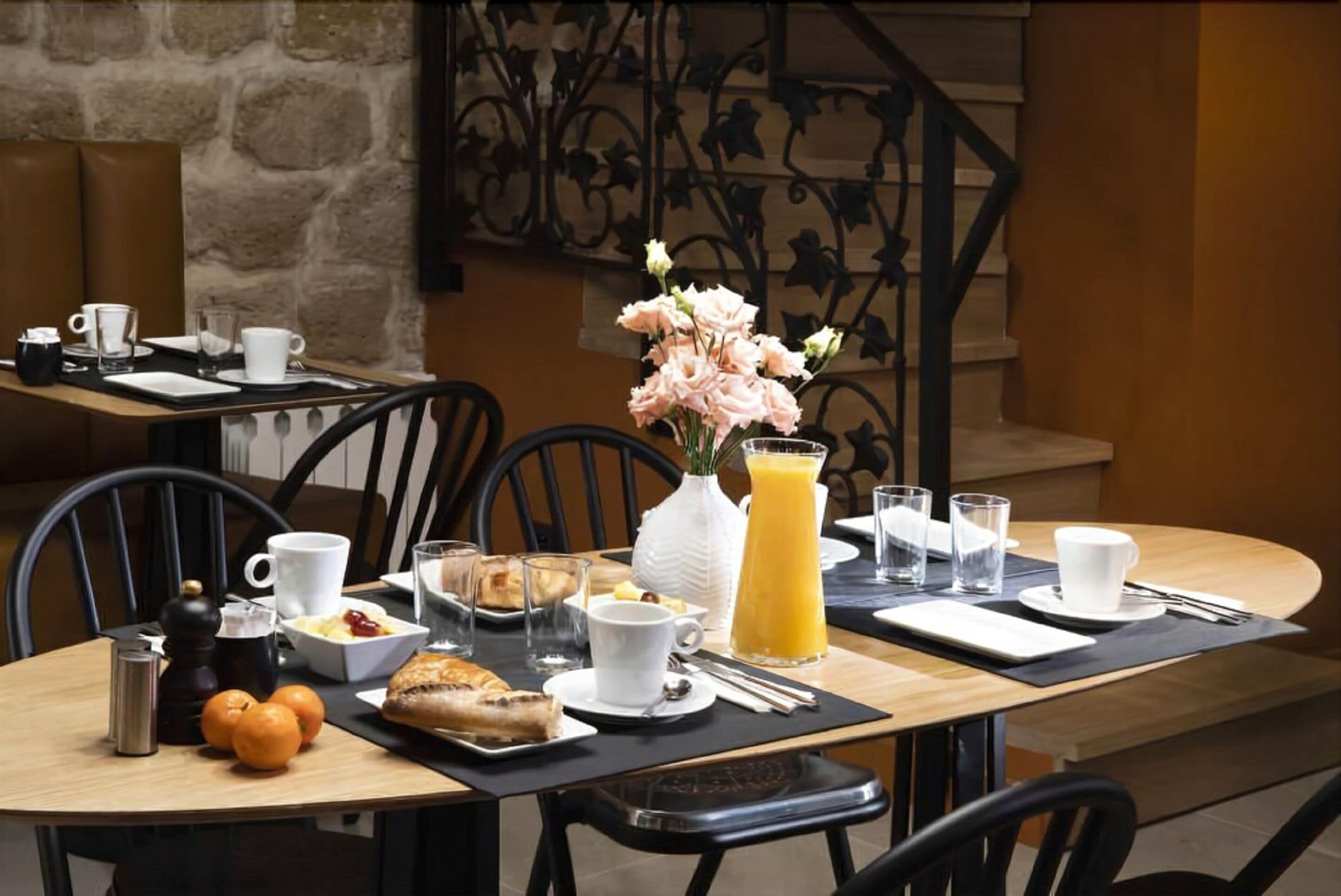 Un desayuno con una mesa para dos, que incluye cruasanes, zumo de naranja y un jarrón con flores.