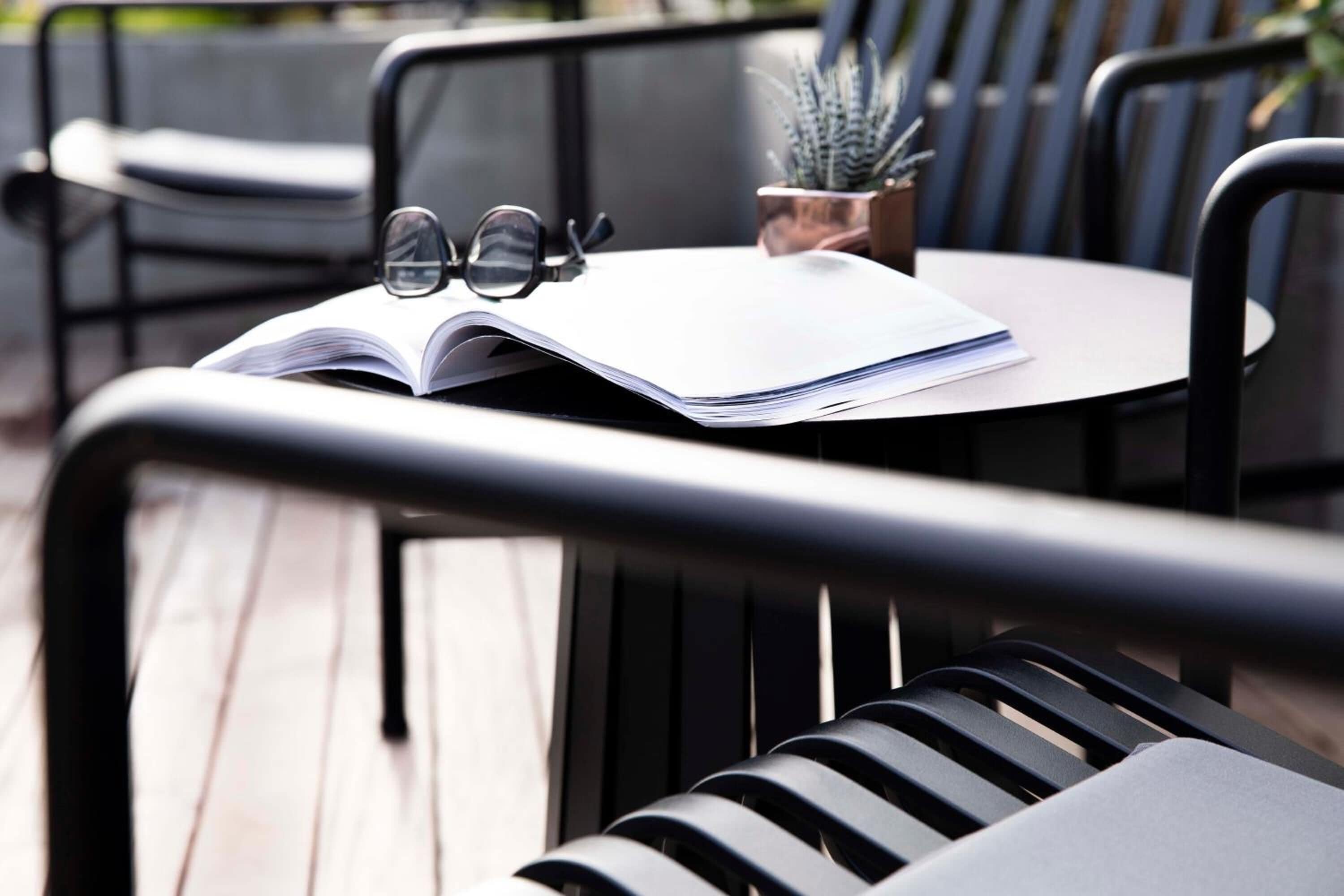 A table with an open book, a pair of glasses, and a small potted plant.