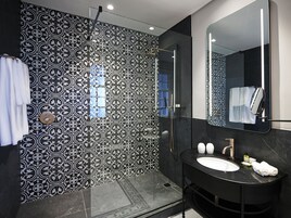 A modern bathroom with a patterned tile wall, a sink with a mirror, and a shower area.