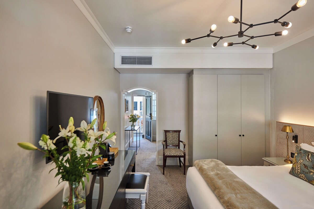 Una habitación de hotel con cama, escritorio con silla, televisión, espejo y candelabro.
