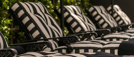 A row of striped lounge chairs with a metal frame, positioned in front of a green leafy background.