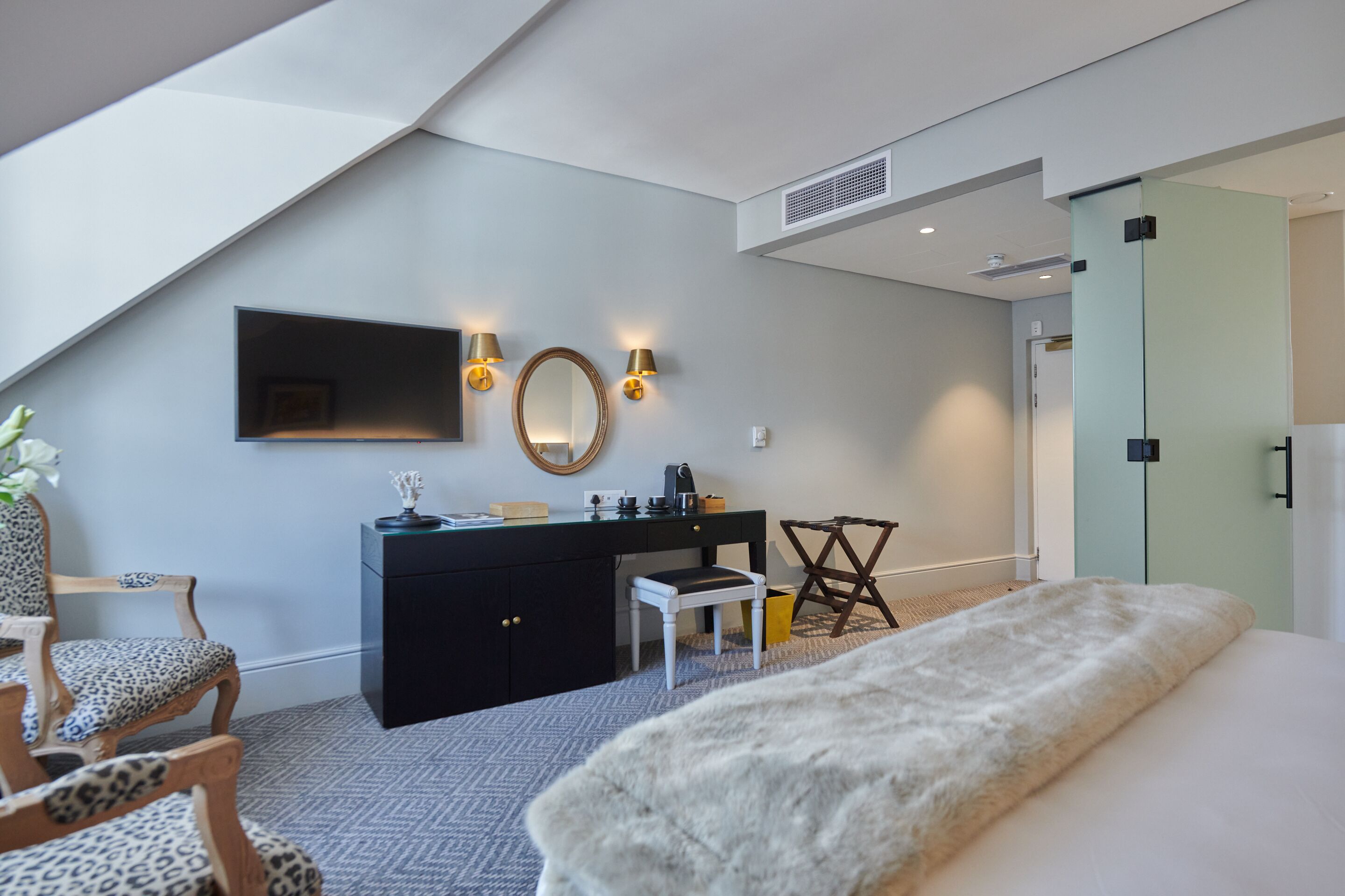 A modern bedroom with a bed, a desk, a chair, a mirror, and wall-mounted lights.
