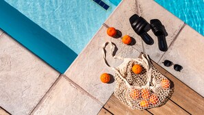 A poolside setting with a tiled edge, a woven bag with oranges, black sandals, and a pair of sunglasses. - The Winchester Hotel by NEWMARK (Cape Town)
