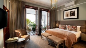 A hotel room with a large bed, a bench, a chair, a TV, and a balcony with curtains. - The Winchester Hotel by NEWMARK (Cape Town)