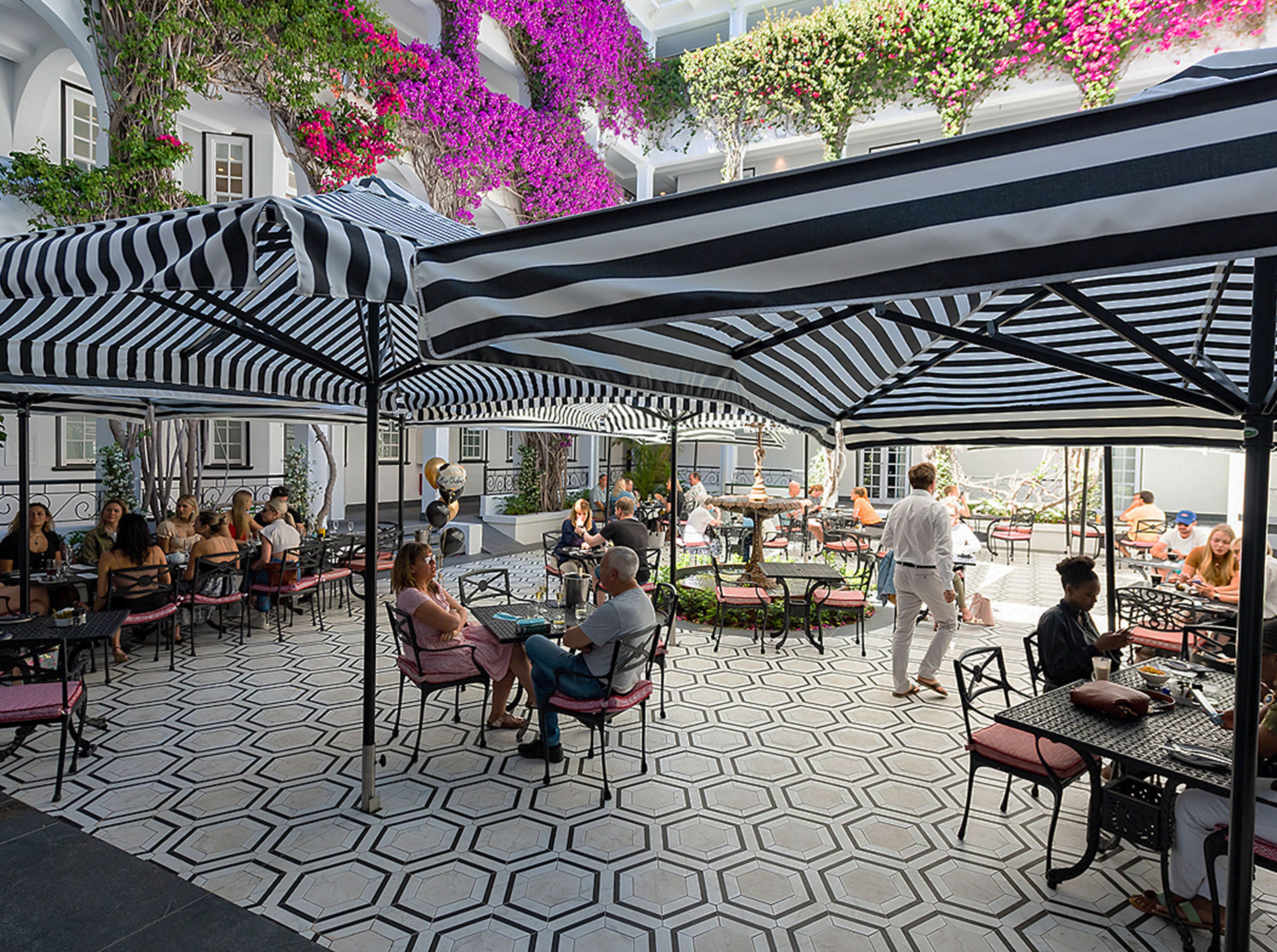 An outdoor café with hexagonal patterned flooring, black and white striped canopies, and people dining.