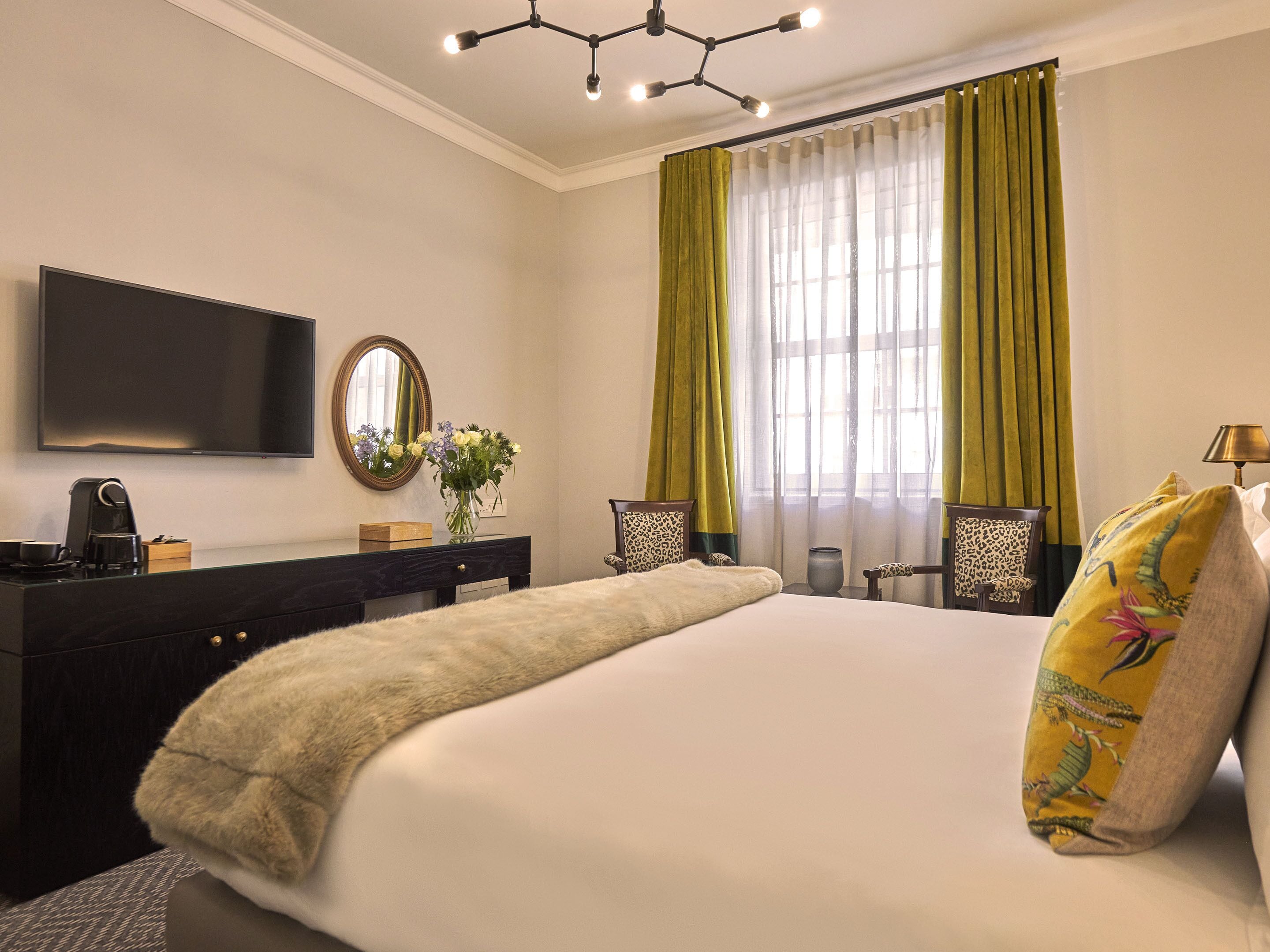 Habitación de hotel con cama, televisión, cómoda, espejo y ventana con cortinas.