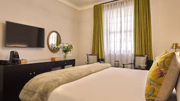 Habitación de hotel con cama, televisión, cómoda, espejo y ventana con cortinas.