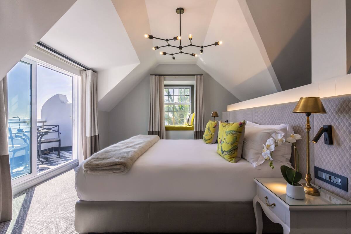 A modern hotel room with a large bed, a bedside table with a lamp, and a view of the balcony.
