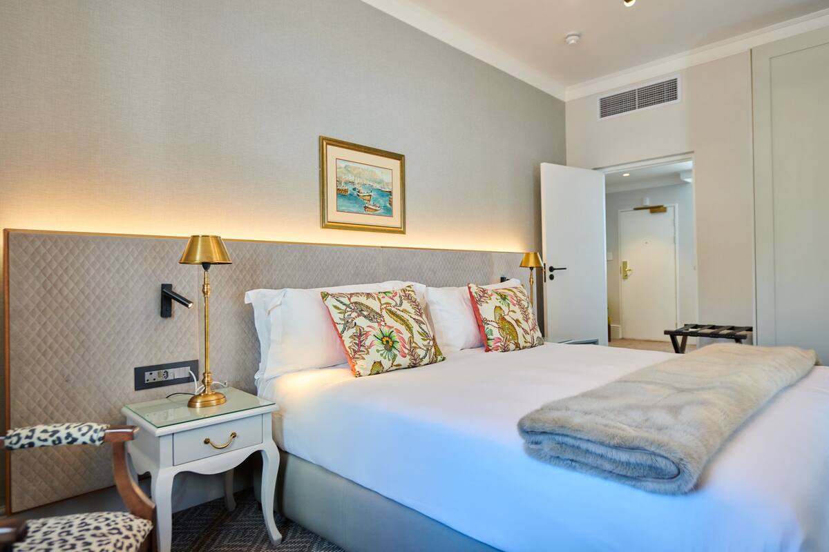 A hotel room with a bed, bedside lamps, a nightstand, a chair, and a door.