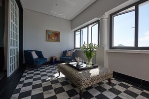 Una sala de estar con piso de cuadros, dos sofás azules, un reposapiés estampado de leopardo y una ventana con vista.