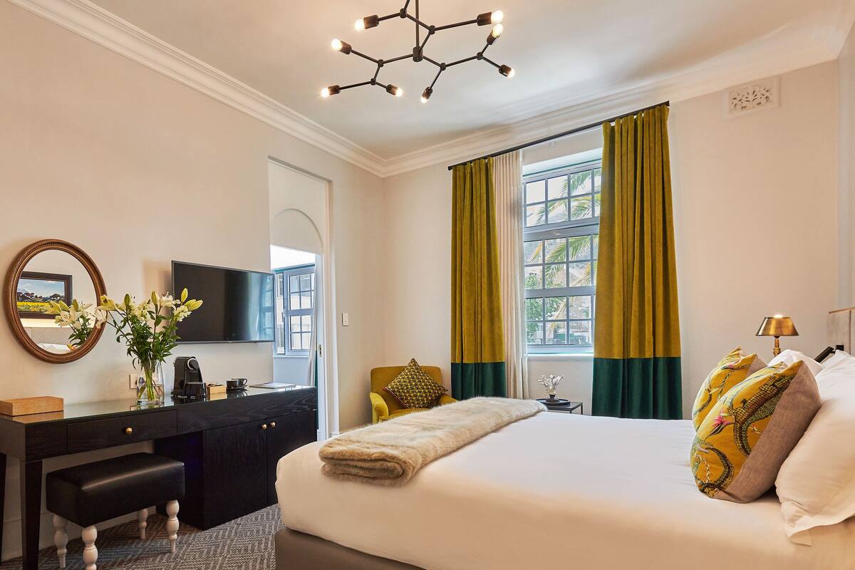 A hotel room with a bed, a desk, a chair, a television, and a window with curtains.