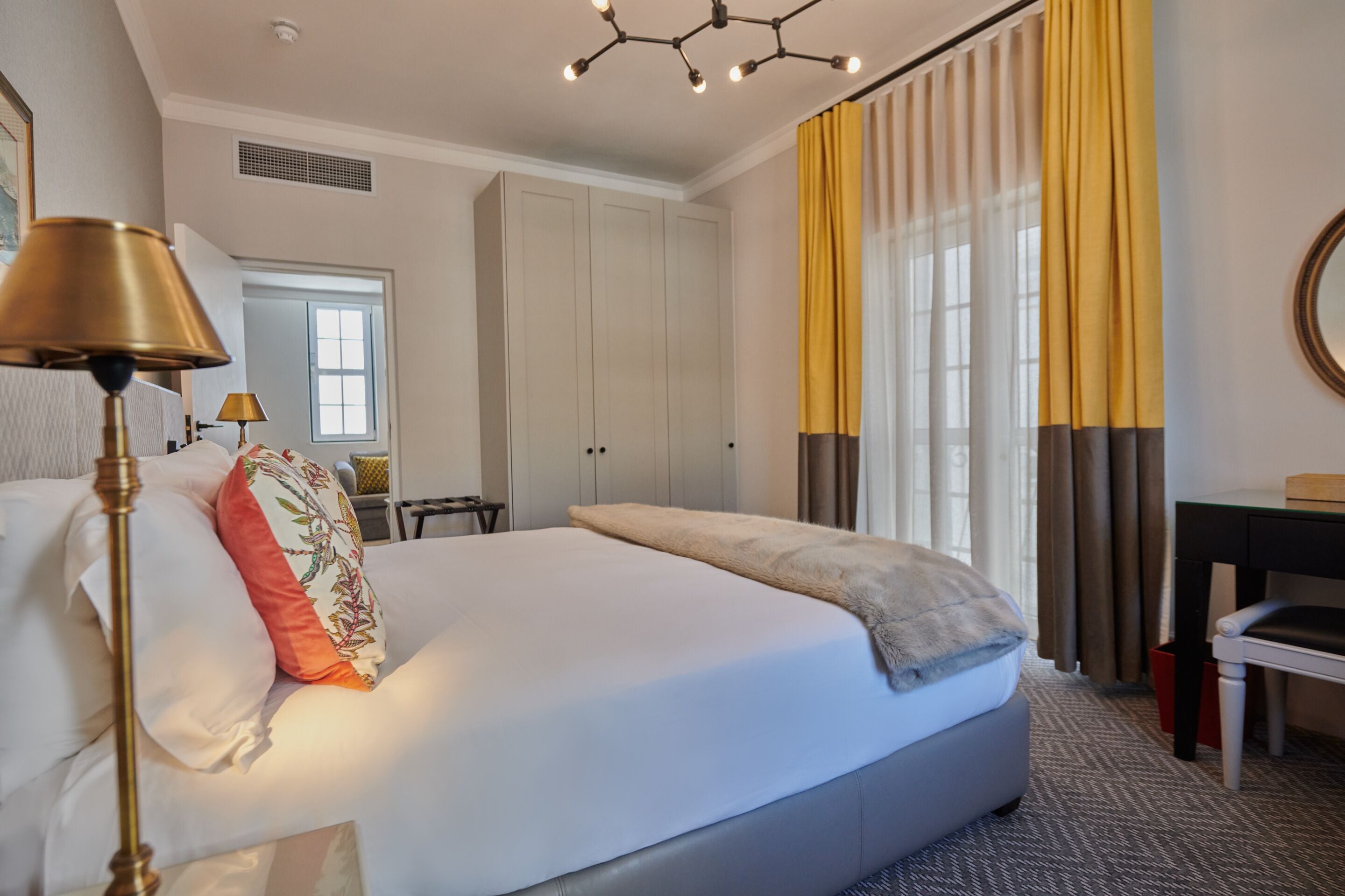 A hotel room with a large bed, a desk, a chair, and a lamp.