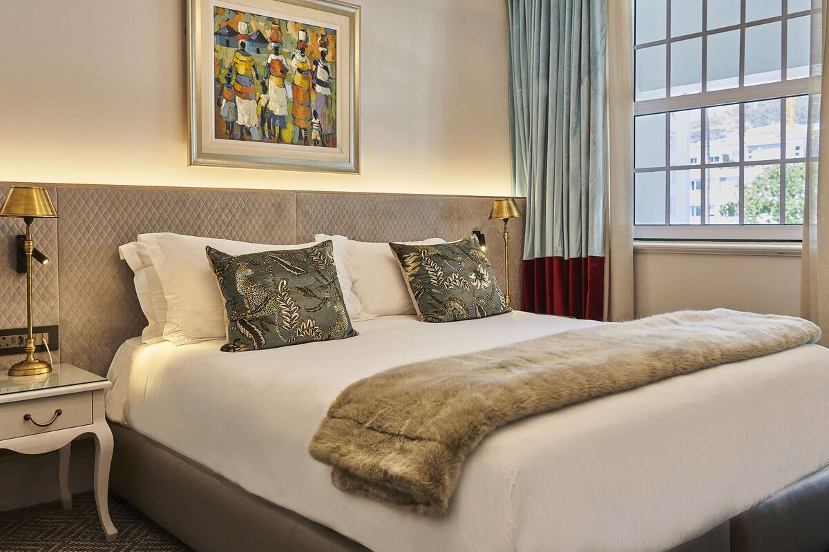 A neatly made bed with a fur throw, two lamps on either side, and a painting above the bed.