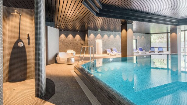 Une piscine intérieure avec un mur carrelé, un plafond en bois et quelques chaises longues.