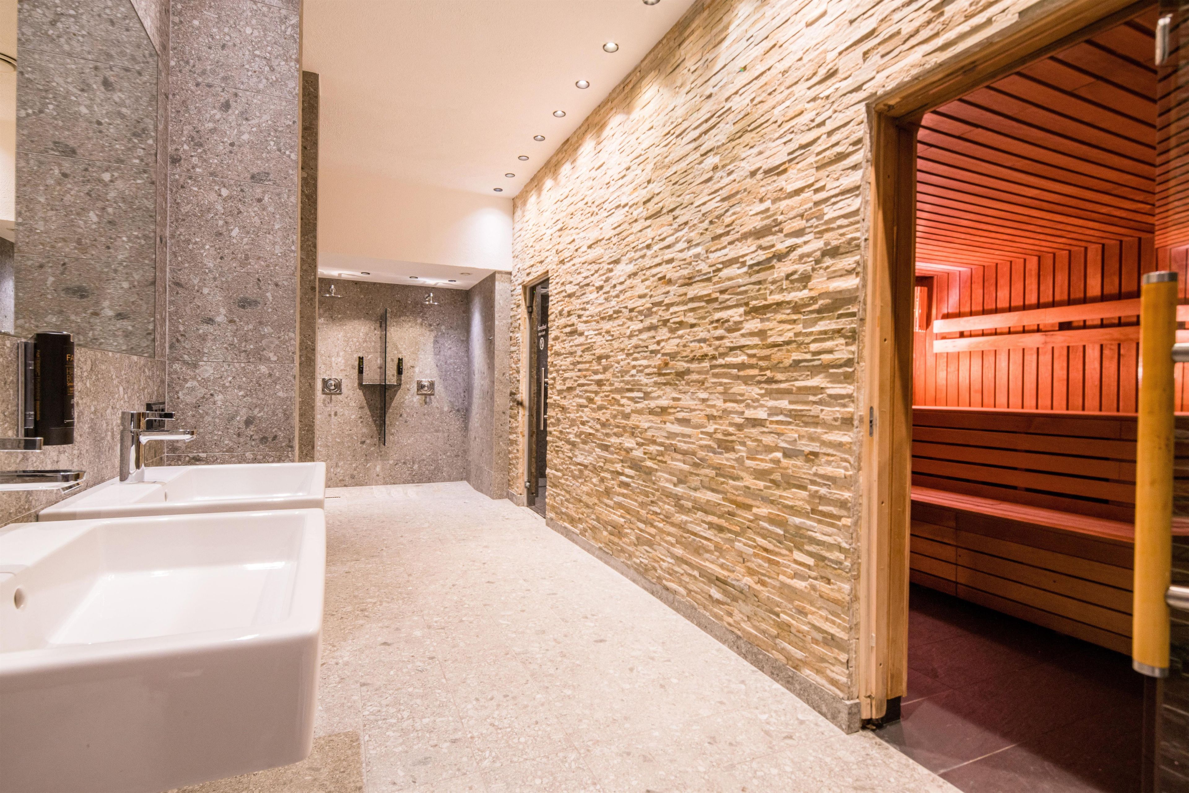 A modern bathroom with a stone wall, a wooden sauna, and a large sink.