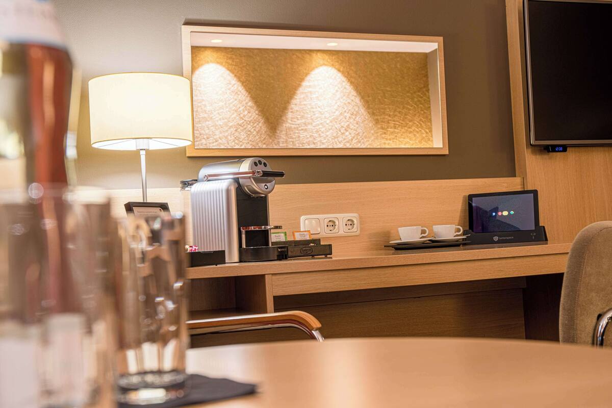 Een hotelkamer met een bureau, een lamp, een koffiezetapparaat, een laptop en een televisie.
