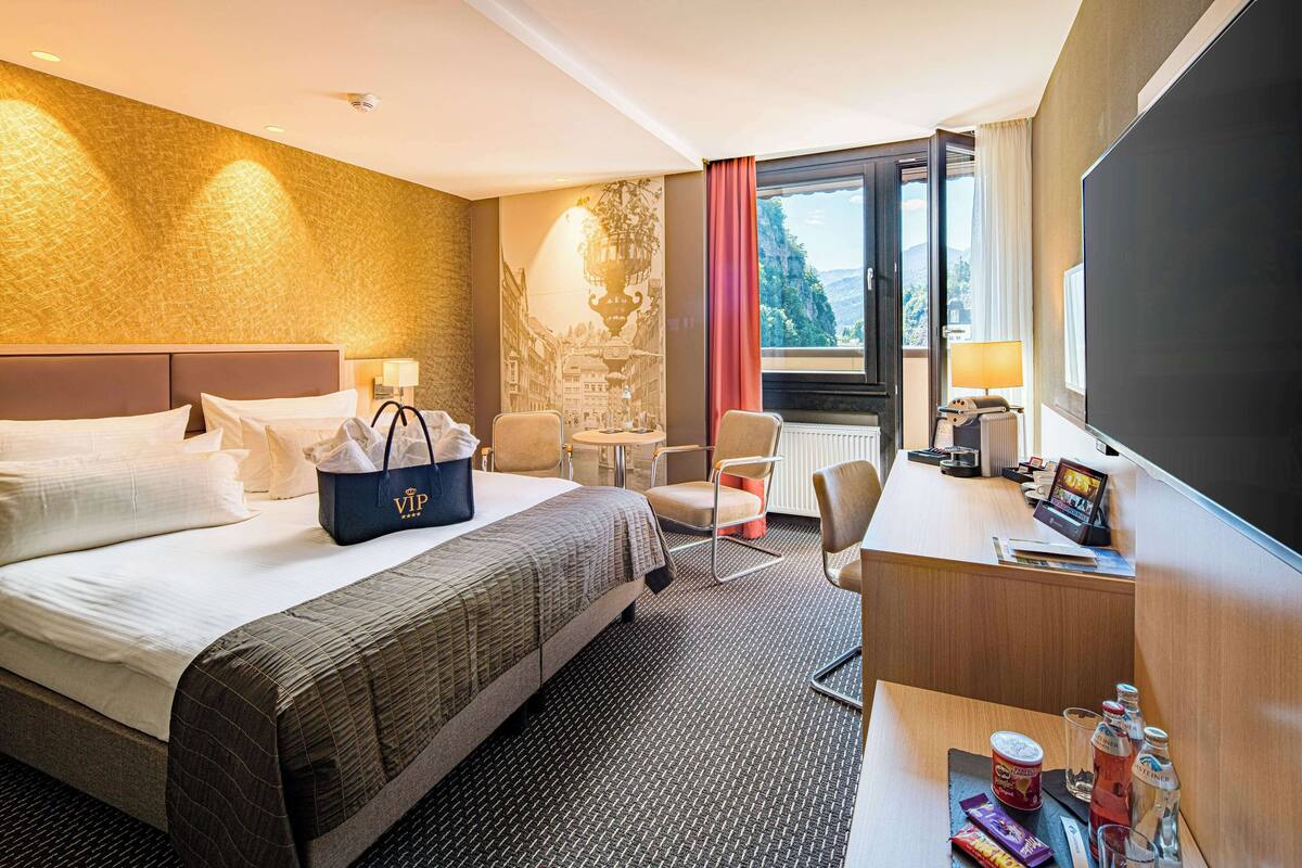 Hotelkamer met een bed, een bureau, een stoel, een televisie en een raam met uitzicht op de omgeving.
