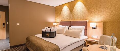 A hotel room with a bed, bedside tables, a desk with a chair, and a wall-mounted lamp.