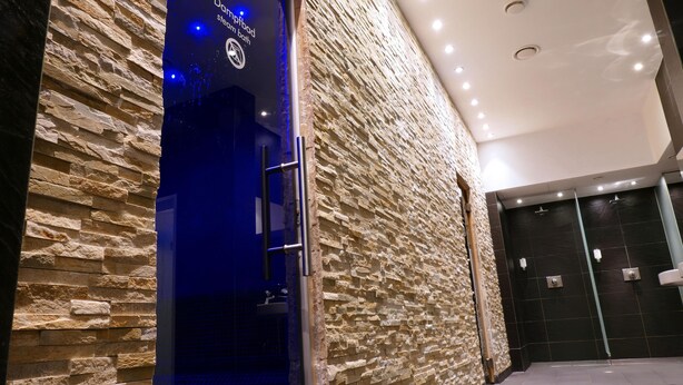 A stone-textured wall with a blue-lit entrance and a black door.