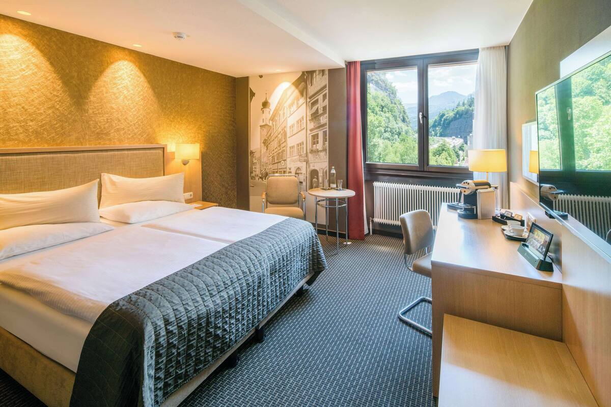 Hotelkamer met een groot bed, een bureau, een stoel, een klein tafeltje en uitzicht op een berglandschap.