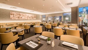A spacious restaurant with multiple dining tables and chairs, large windows, and a modern interior design.