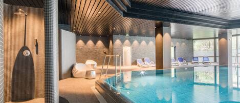 A modern indoor swimming pool with a clear water surface, a wooden ceiling, and a brick wall.