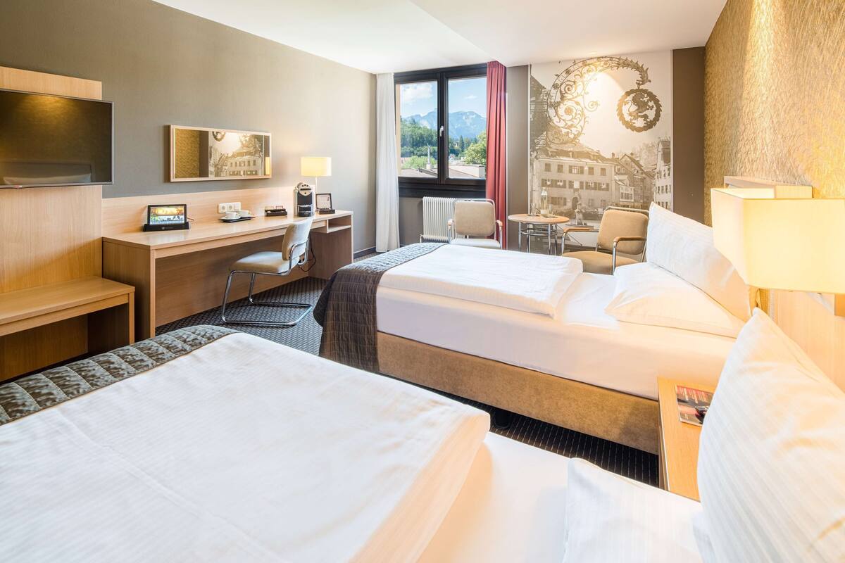 Hotelkamer met twee bedden, een bureau, een stoel, een televisie en een raam met uitzicht.