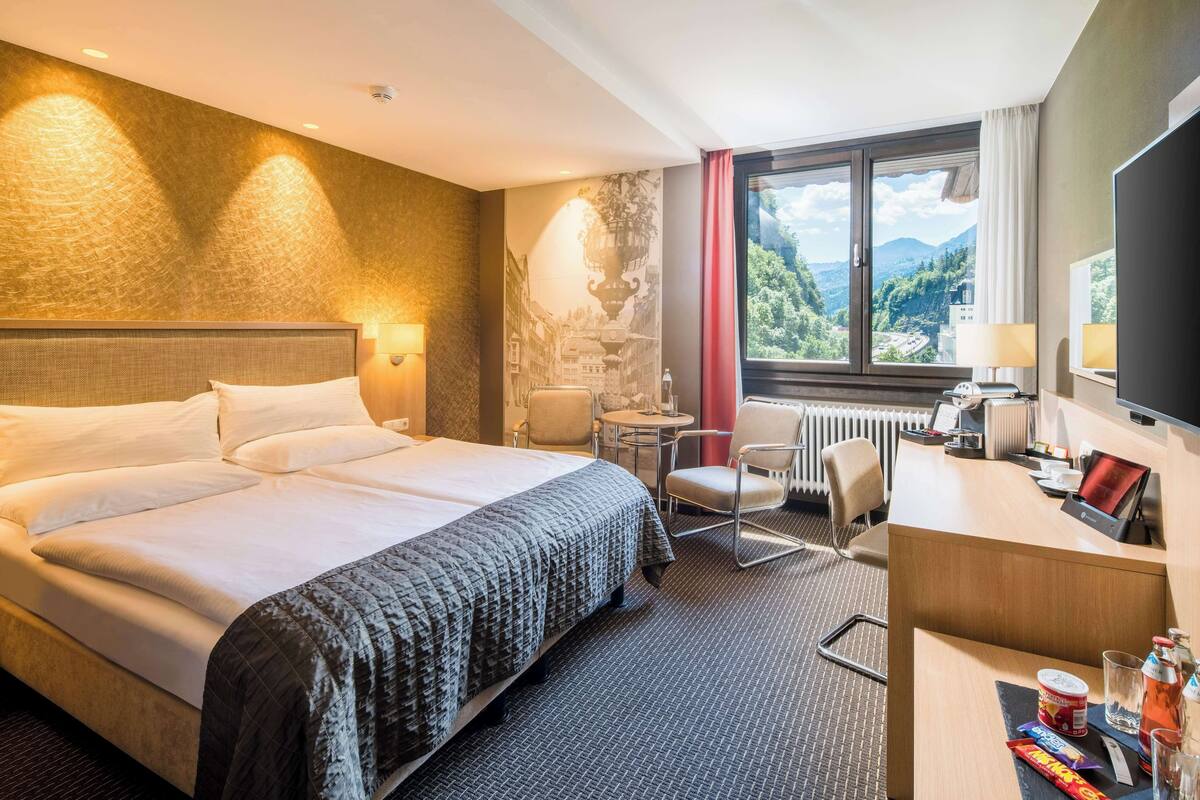 Een hotelkamer met een groot bed, een bureau, een stoel en uitzicht op de bergen.