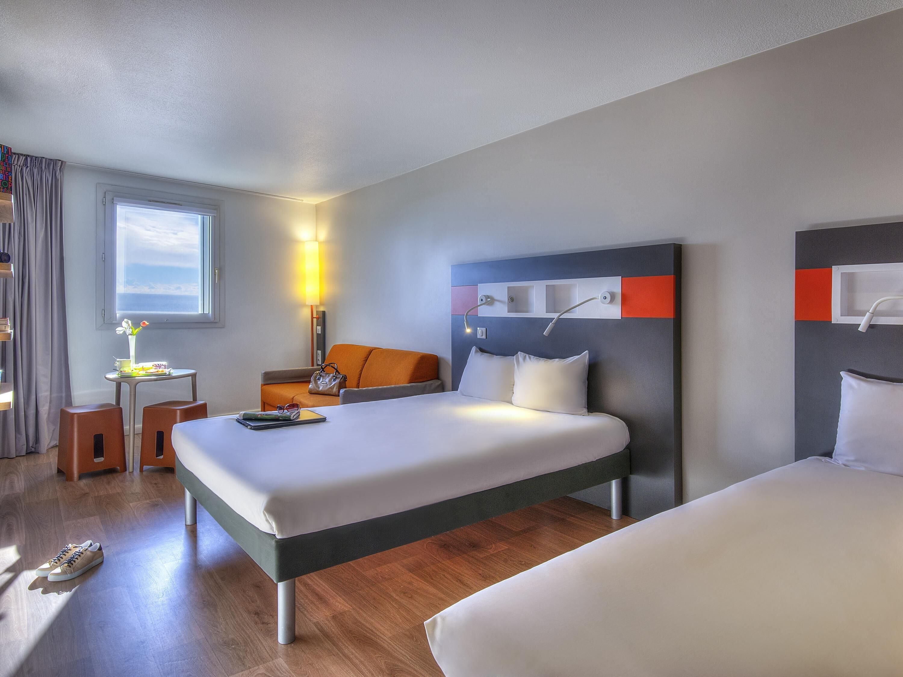 A hotel room with a bed, bedside tables, a desk, a chair, and a window.