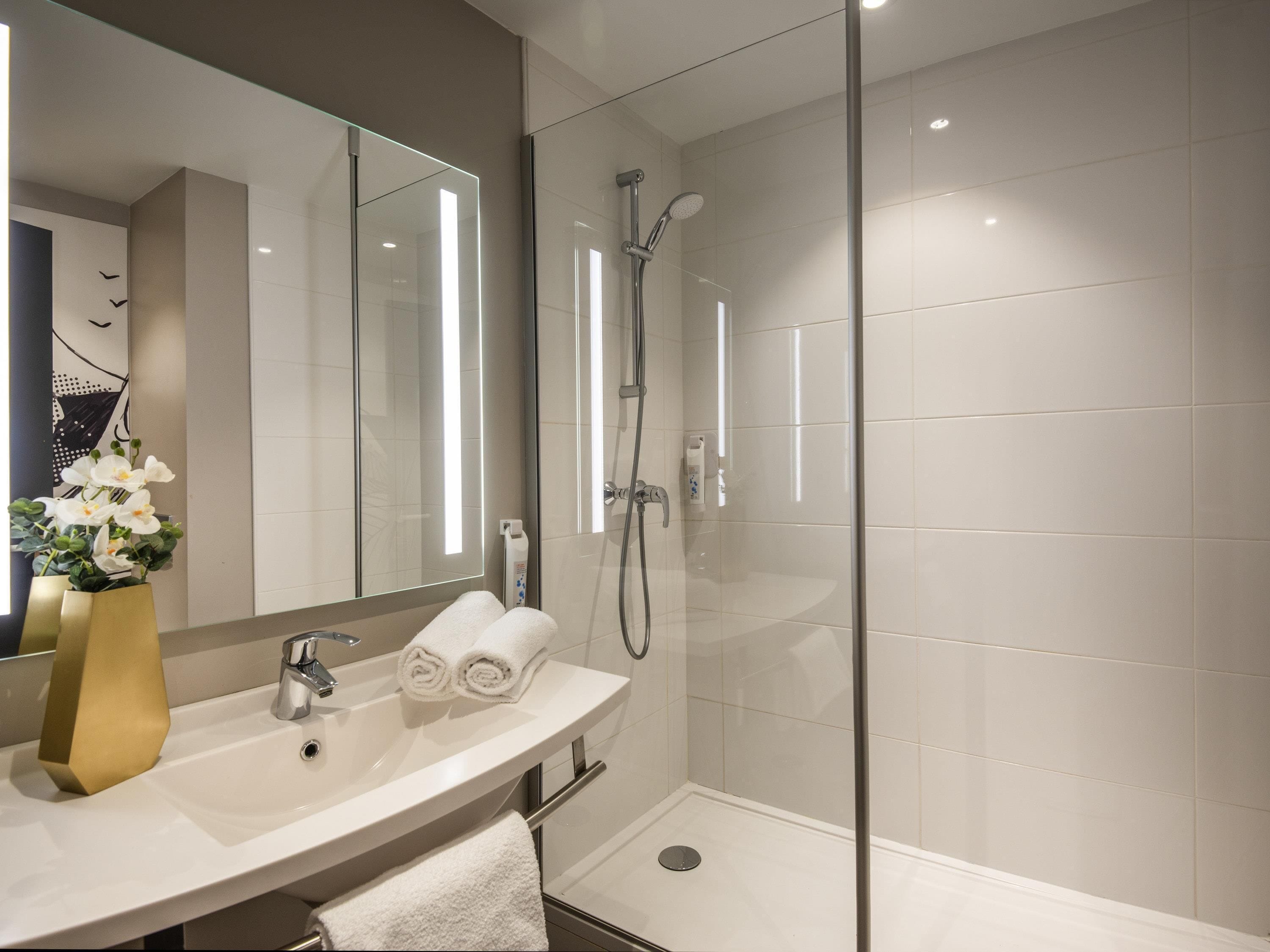 A modern bathroom with a glass-enclosed shower, a sink with a mirror, and a vase with white flowers.