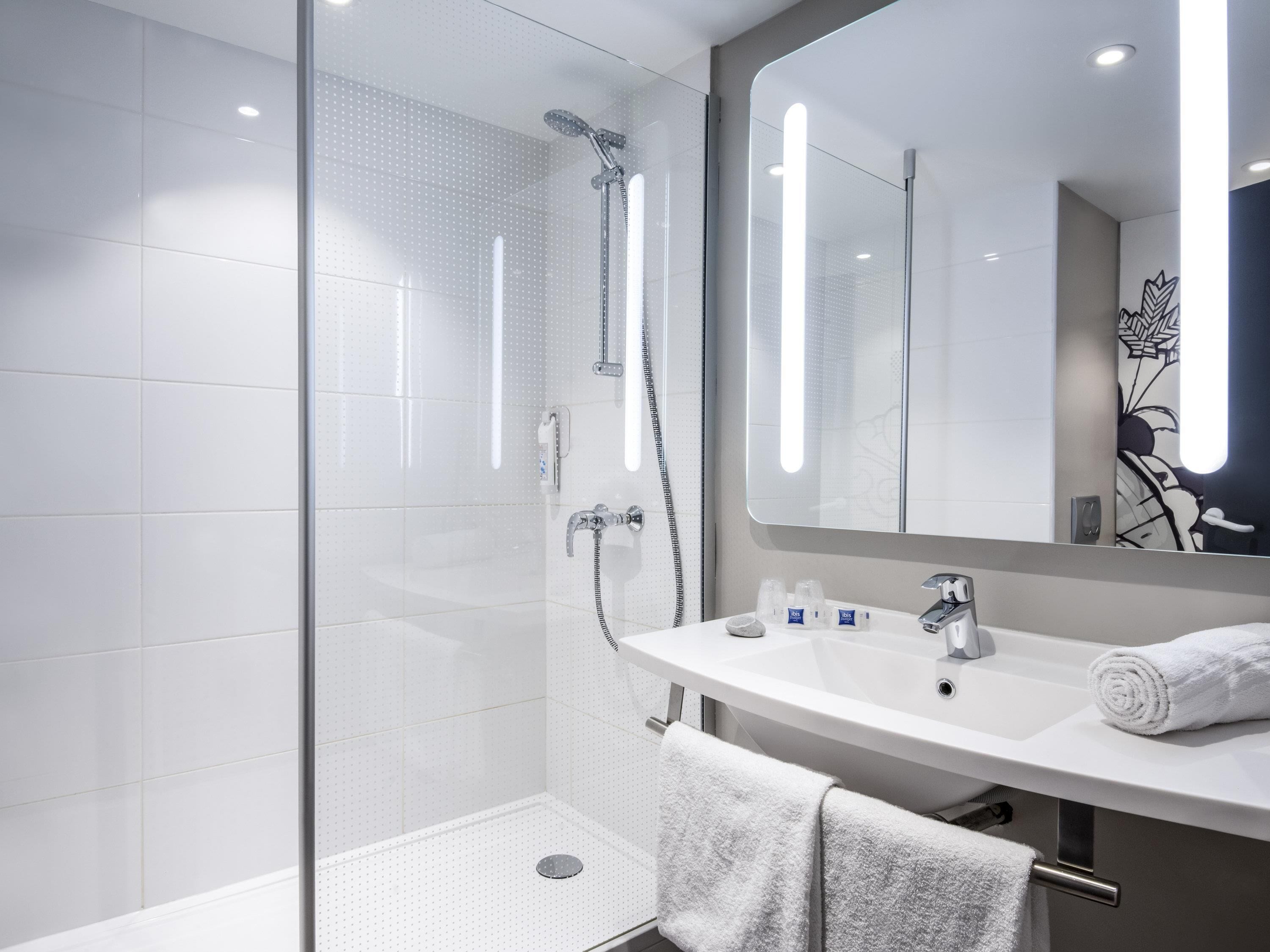 A modern bathroom with a glass-enclosed shower, a white sink, and a large mirror.
