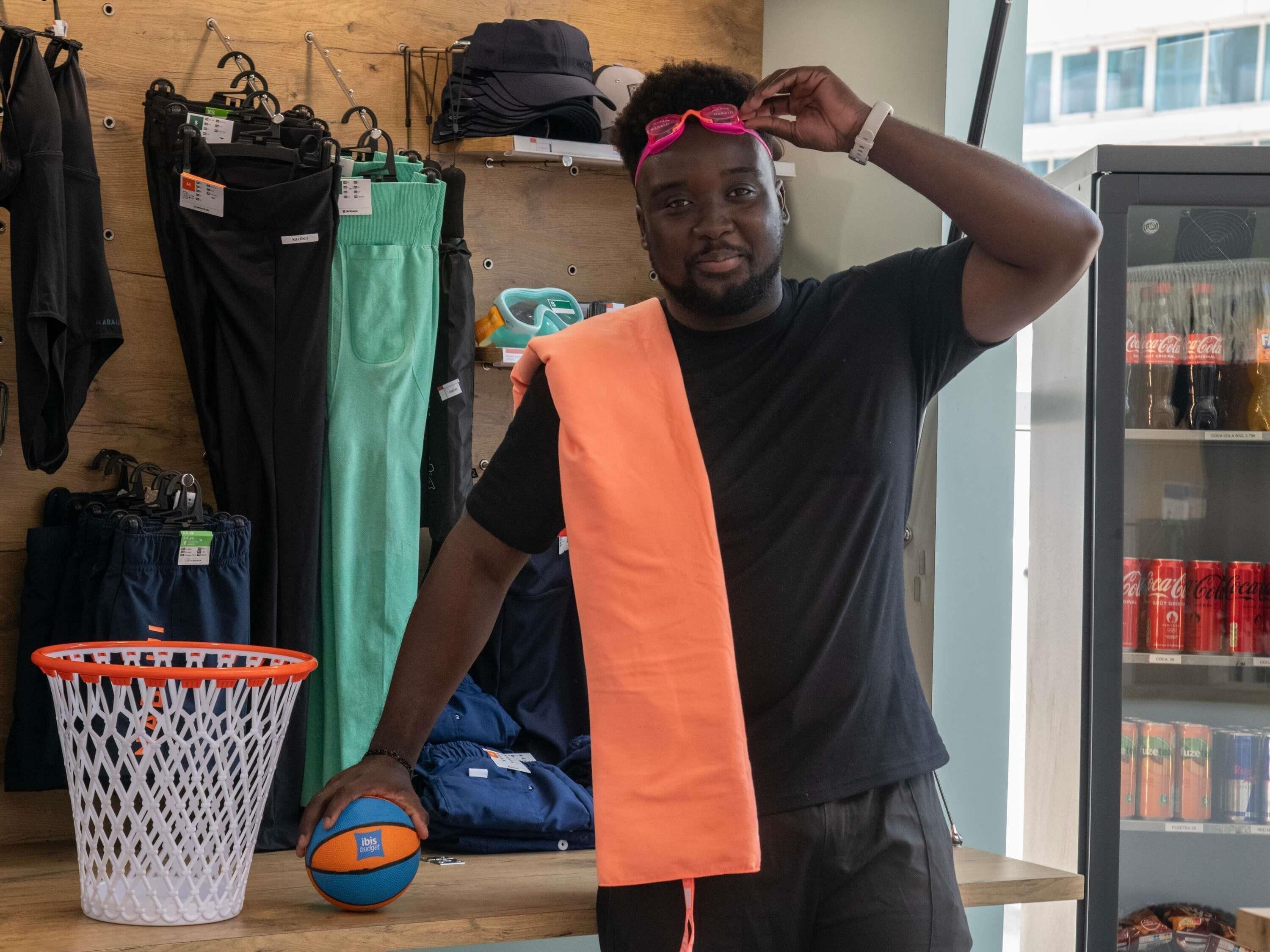 A person holding a basketball and a towel in a store with clothing racks and a beverage refrigerator.
