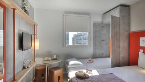 Ein modernes Hotelzimmer mit einem Bett, einem kleinen Schreibtisch, einem Fernseher und einem Fenster mit Blick auf die Stadt.