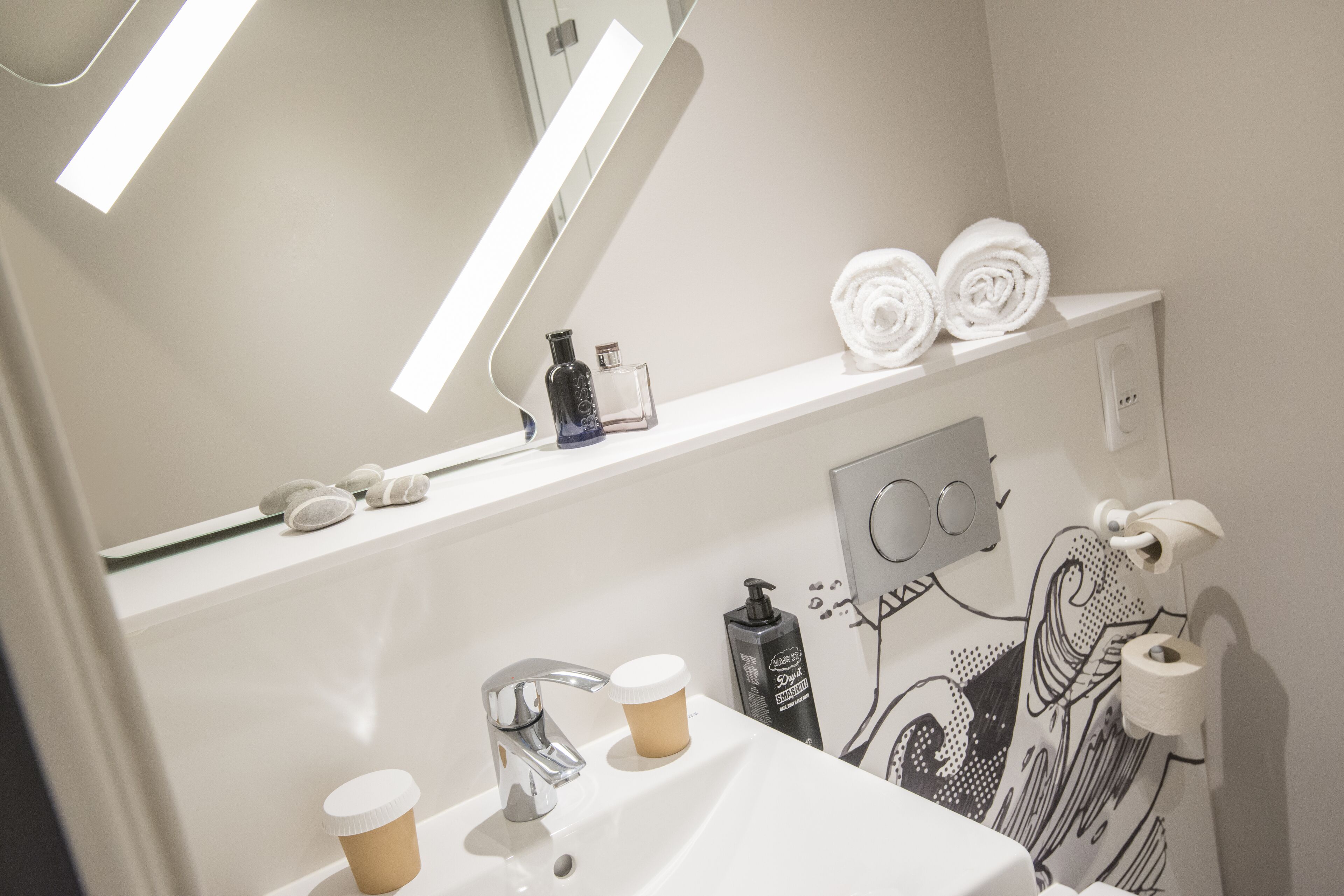 A bathroom with a white sink, a mirror, and a shelf with towels and toiletries.