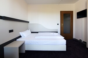 Una habitación de hotel con una cama, una mesita de noche y una puerta.
