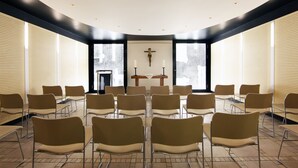 A modern chapel with a curved ceiling, rows of chairs, and a central altar with candles. - Dietrich-Bonhoeffer-Hotel (Berlin)