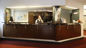 A reception desk with a person behind it, a bookshelf, and a sign labeled "BMZ". - Dietrich-Bonhoeffer-Hotel (Berlin)