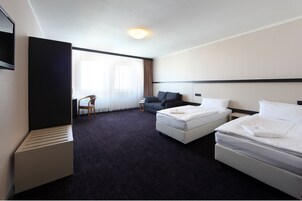 Une chambre d’hôtel avec deux lits, un bureau, une chaise et une grande fenêtre avec des rideaux légers.