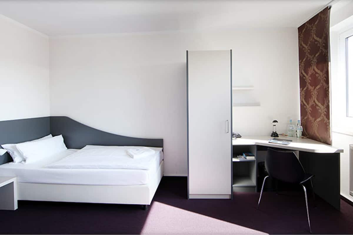 A modern hotel room with a bed, desk, chair, and a large window.