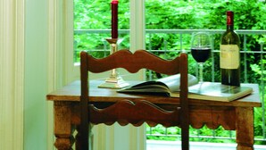 A dining table with a book, two candles, and a bottle of wine, set against a window with a view of lush green trees. - Hotel Miramar (Hamburg)