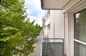 A narrow pathway flanked by trees and a building with balconies. - acora Leipzig Living the City (Leipzig)
