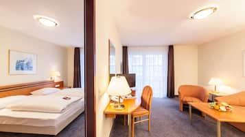 Quarto de hotel com cama, escrivaninha, cadeira e uma pequena mesa com abajur.
