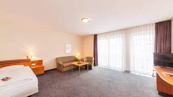 A hotel room with a bed, a sofa, a small table with fruit, a TV, and a window with curtains.