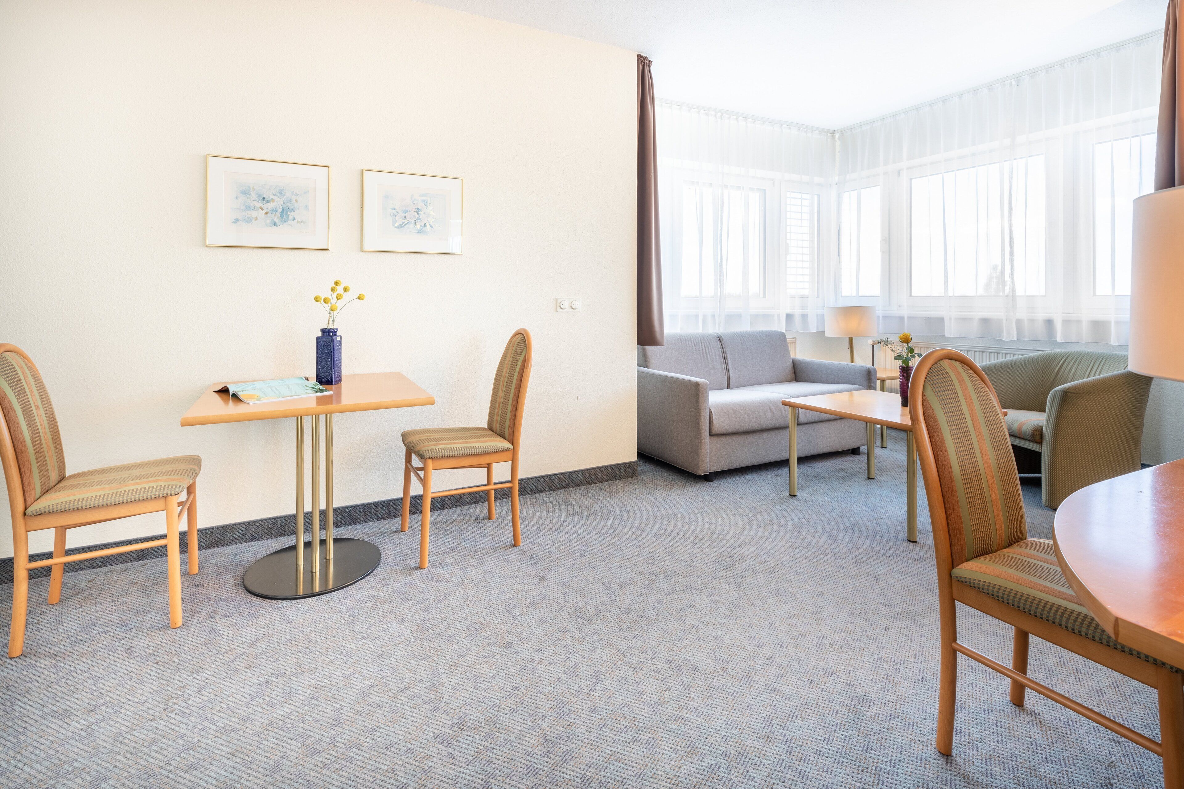 Een hotelkamer met een zithoek, een bank en een stoel. Twee ingelijste foto's hangen aan de muur.