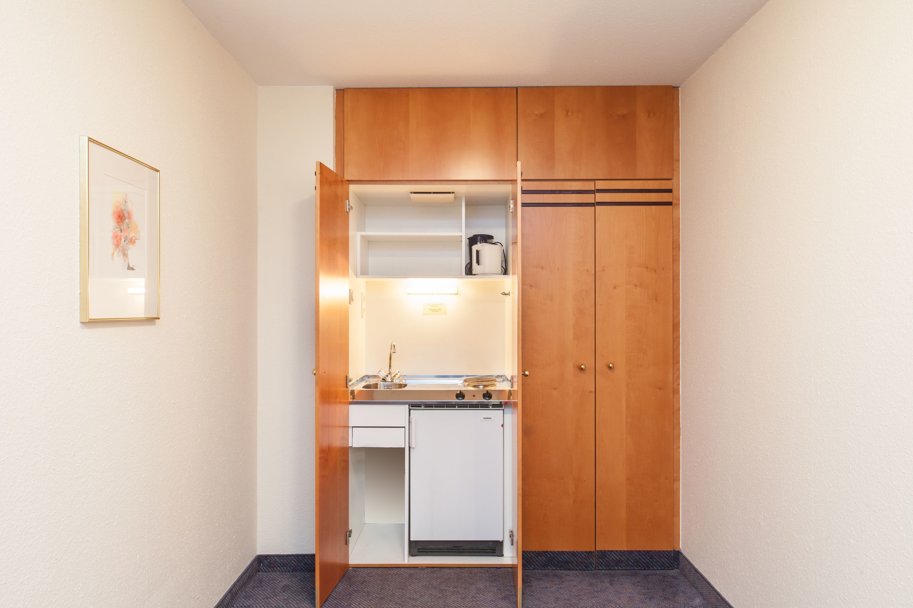 Eine kompakte Küchenzeile mit Einbauherd, kleinem Kühlschrank und Spüle.